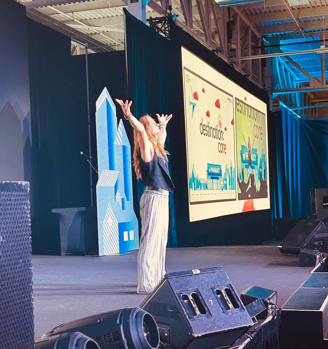 Michelle on stage at a Loblaw / Shoppers conference, arms raised in front of a large screen