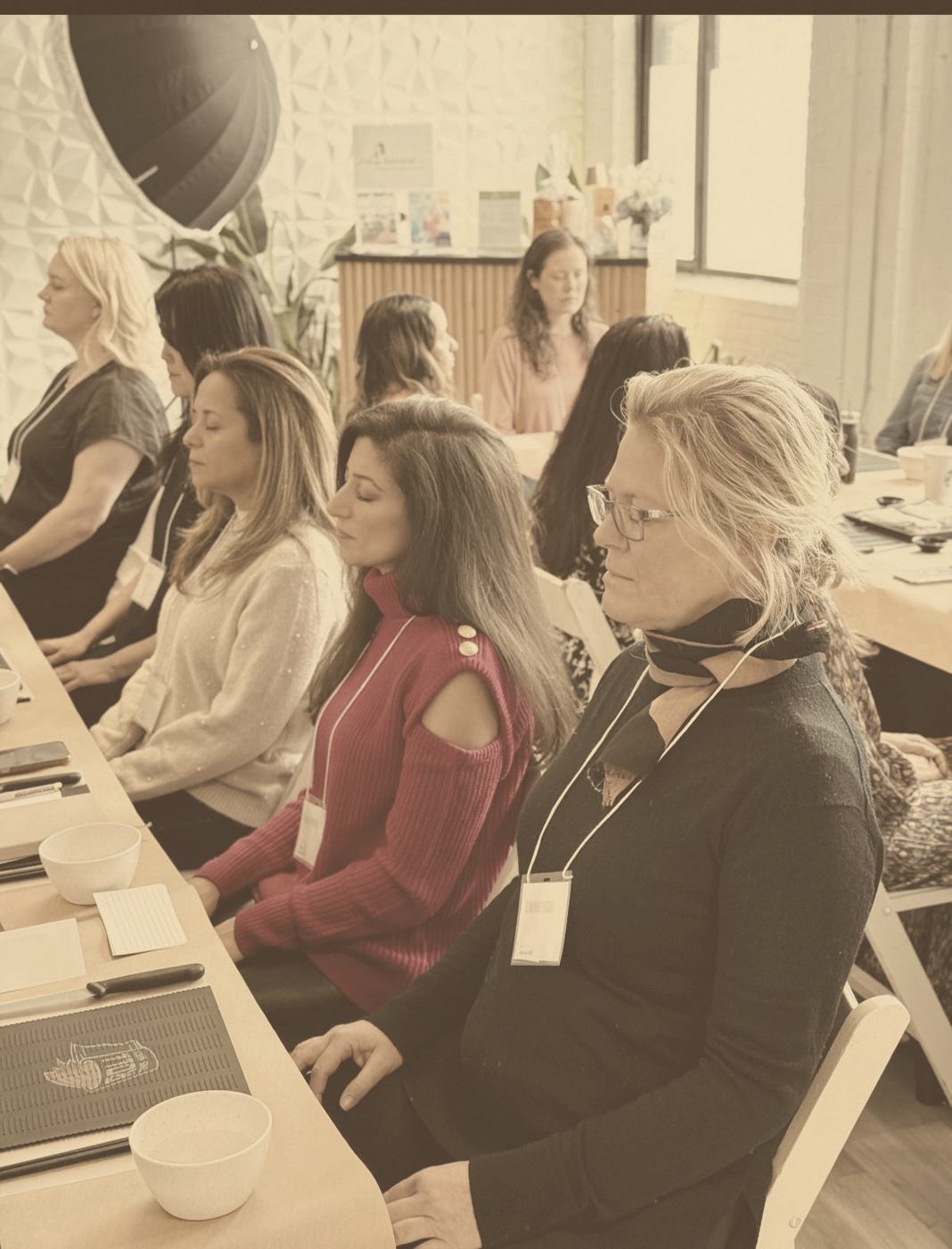 Participants seated at a long table, eyes closed, in a professional learning session